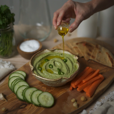 cilantro serrano hummus being topped with evoo