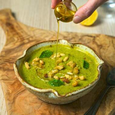 Drizzling olive oil over creamy pesto soup.