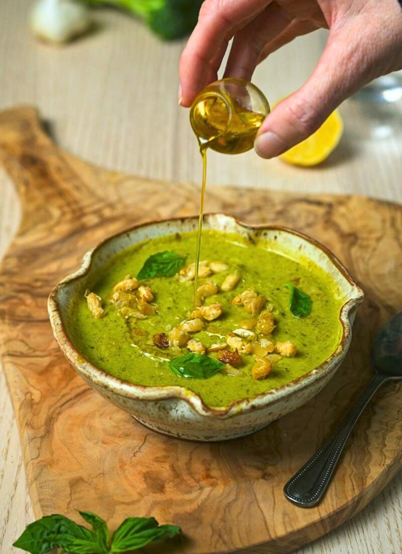 Drizzling olive oil over creamy pesto soup.