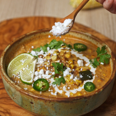 sprinkling cheese on top of elote soup