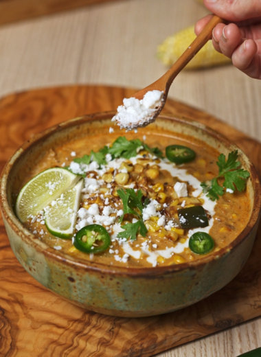 sprinkling cheese on top of elote soup